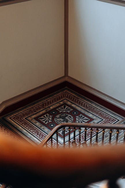 An interior view of a narrow, winding staircase inside a Victorian-style residential property, featuring cream-painted walls and dark wooden handrails with decorative balusters. The staircase has a cu